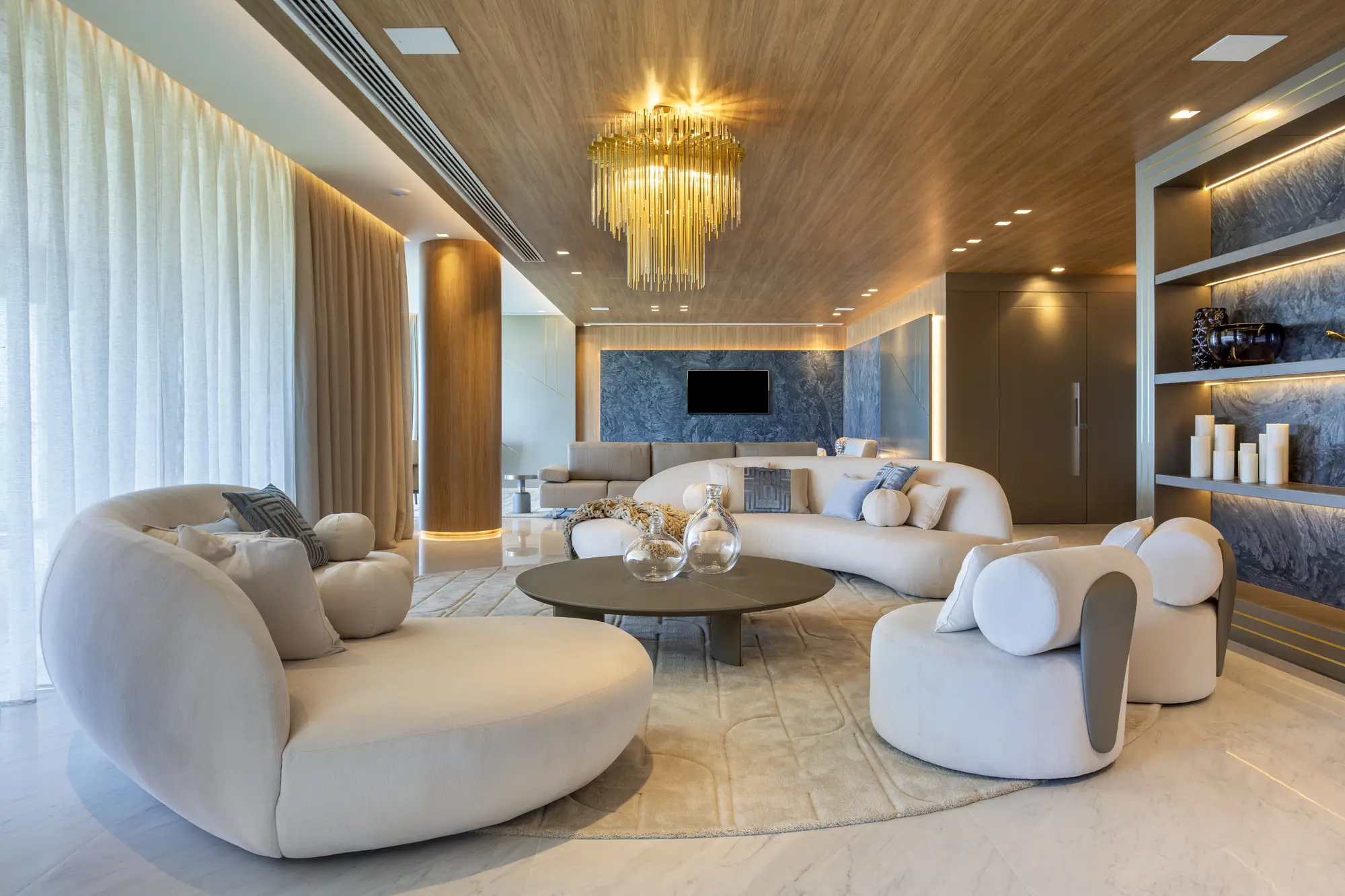 Living com sofás curvos, lustre de cristal e estantes iluminadas em pedra